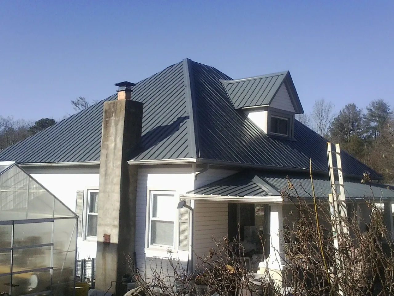 Dark blue standing seam metal roof on a white farmhouse with dormer — Slate & Tile Roof Repair by Roofing Brothers in Peosta