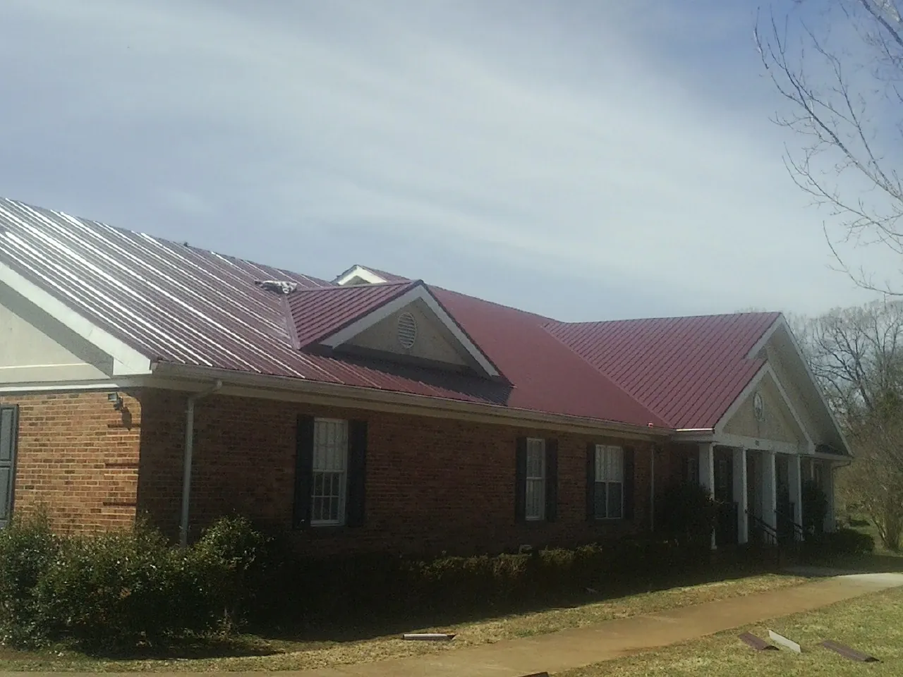 Red metal roof with gabled entries on a long brick building, from a Hail Damage Roof Repair job in Peosta