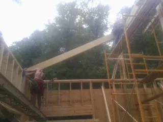 Carpenter raising a rafter beam on a new second story frame in Peosta