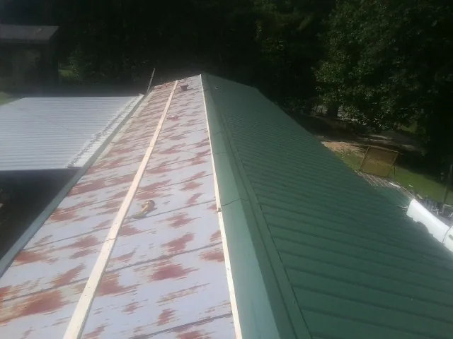 Old rusted panels beside newly installed green metal roofing — Wind Damage Roof Repair by Roofing Brothers in Peosta
