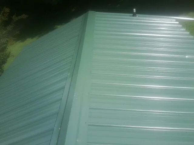 New green metal panels meeting at the ridge of a roof — Flat Roof Repair work by our crew in Peosta