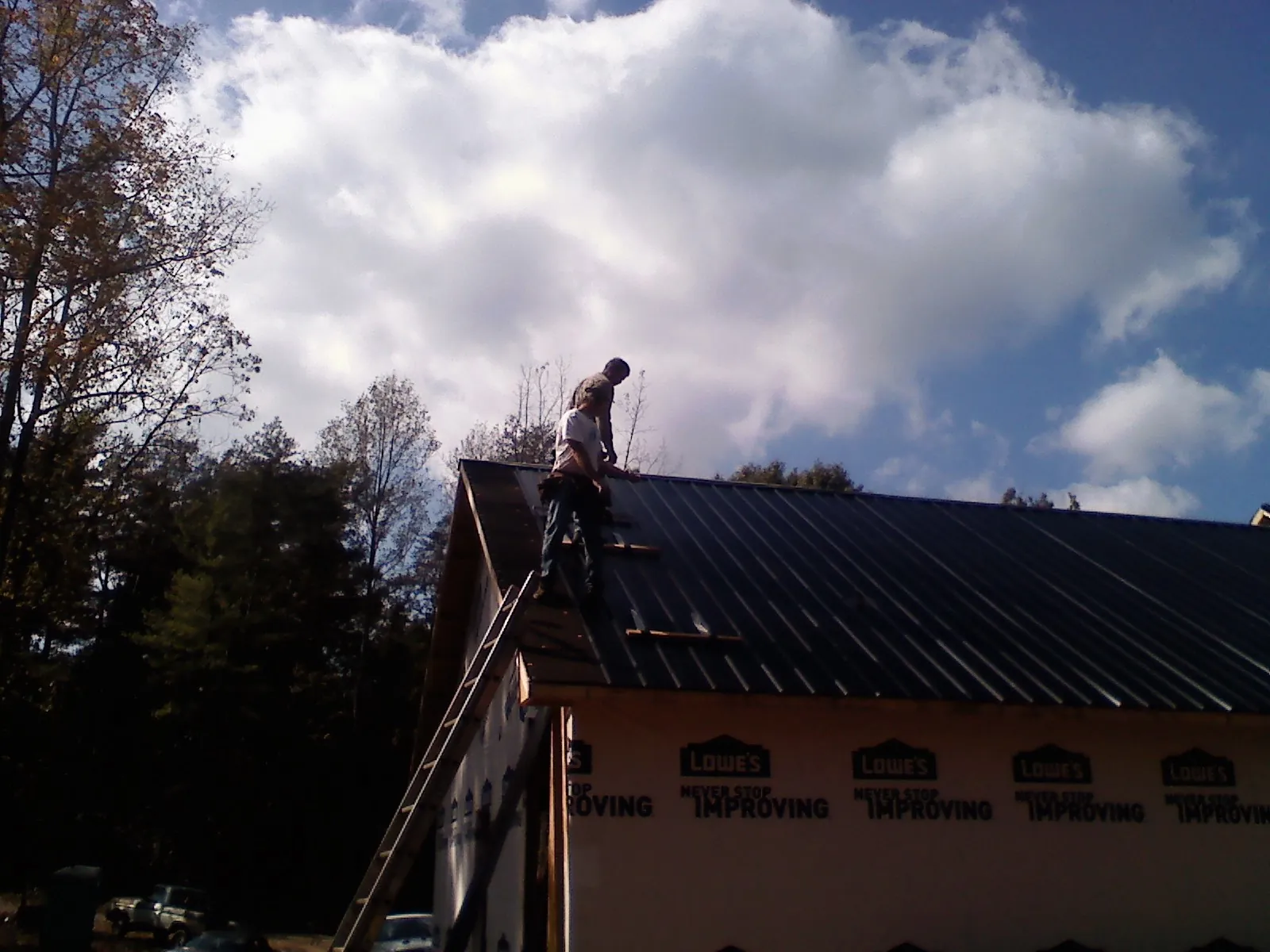 Roofer fastening dark metal panels high against a cloudy sky, from a Roof Inspection job in Peosta