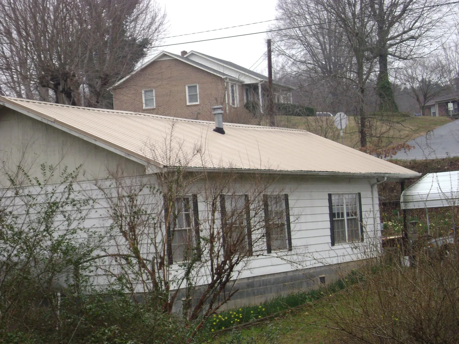 Tan metal roof on a white sided house set into a hillside — Commercial Roofing by Roofing Brothers in Peosta