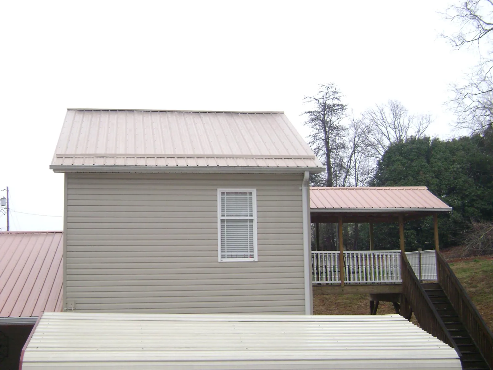 Tan metal roofs on a two story addition and attached porch, from a Roof Replacement job in Peosta