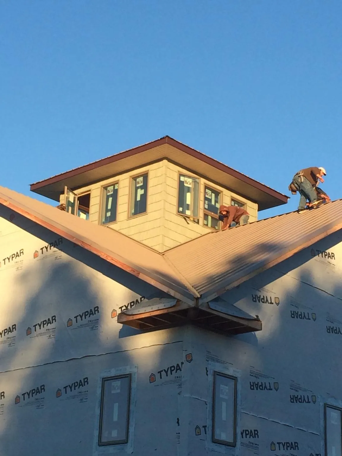 Roofers working around a rooftop cupola on a new metal roof at sunset — Roof Waterproofing in Peosta by Roofing Brothers
